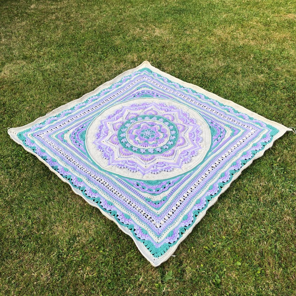 Image of a crochet blanket in colours of violet, Wisteria, green and parchment.